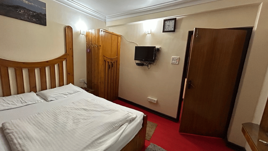 Room with a double bed, wooden furniture, a wardrobe, and a television mounted on the wall at Hotel Dolphin Darjeeling.