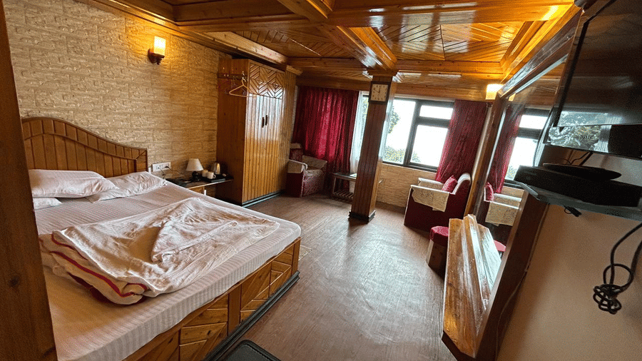 Spacious room with a double bed, red and wood decor, a mirror, and a view through a balcony door at Hotel Dolphin Darjeeling.