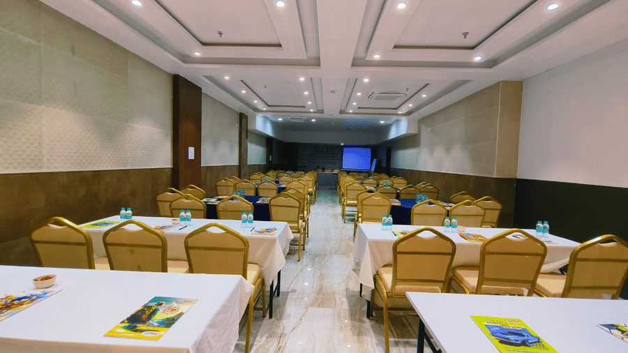 Conference-style hall at Hotel Mumbai House, Vashi with rectangular tables, chairs and a screen at the front.