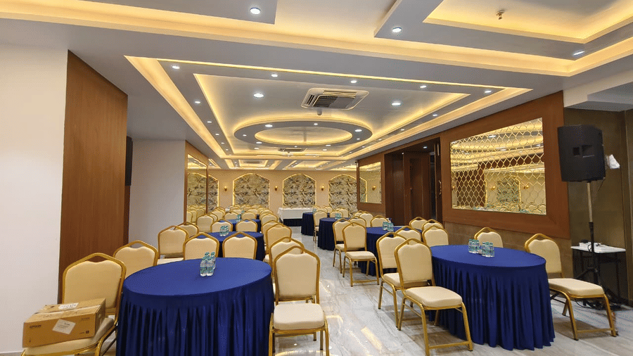 Spacious banquet area at Hotel Mumbai House, Vashi featuring round tables, chairs and decorative ceiling lighting.