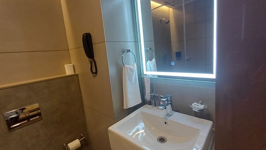 Image of a restroom wiith sink and lighted mirror at Hotel Raai, Hosur.