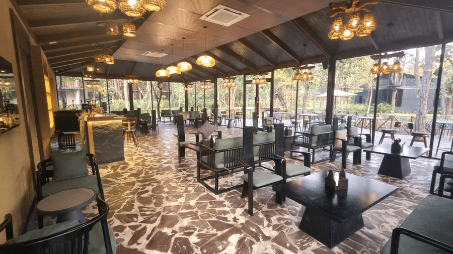 Large windows in the dining area at Hotel Sonar Bangla Joypur Forest, Bankura offer views of the surrounding greenery.