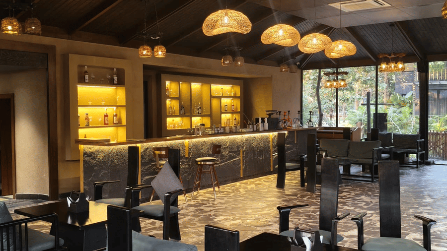 A stylish bar area with backlit shelving serves as a focal point at Hotel Sonar Bangla Joypur Forest, Bankura.