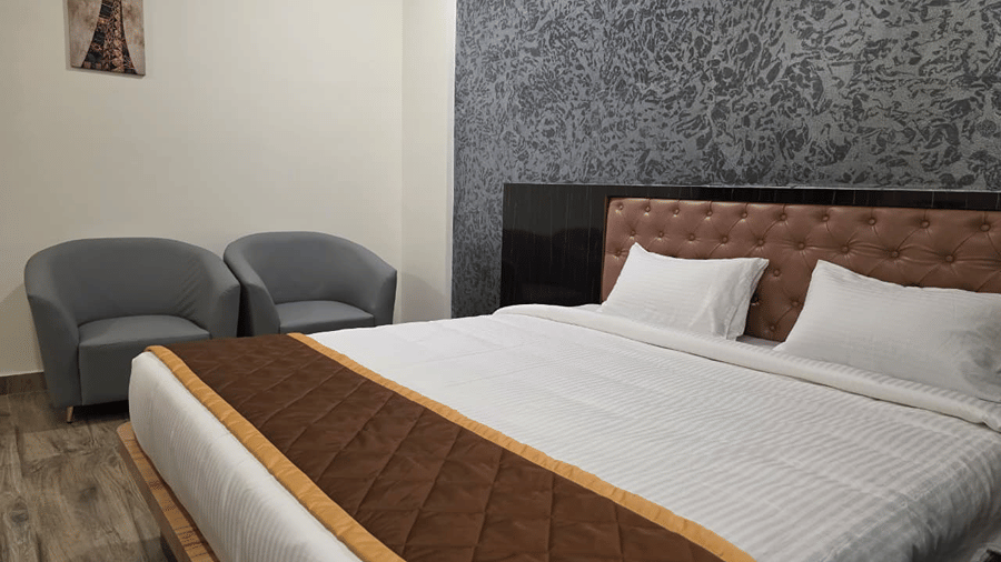 edroom with a king size bed featuring a brown bedspread, paired with two grey chairs near the window.