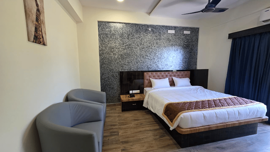 A bedroom with a king size bed, grey armchairs, wooden flooring, and a patterned wall piece above the headboard.