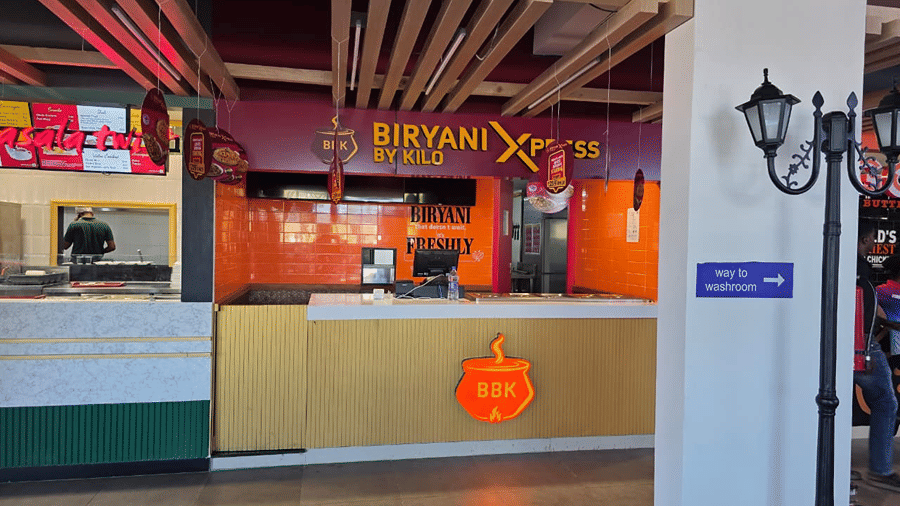 A food counter serving biryani, seen alongside a decorative lamp post and orange coloured signage.