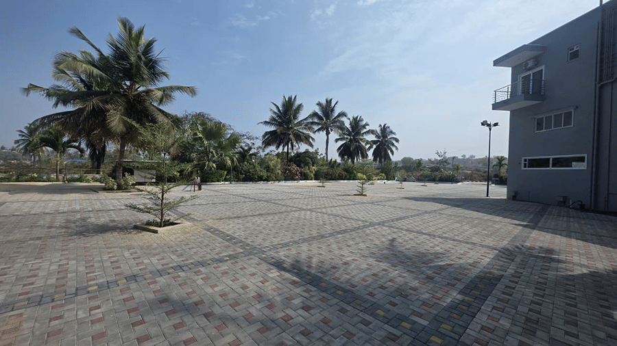 An open stone courtyard with palm trees and a grey building standing in the background under a bright sky.
