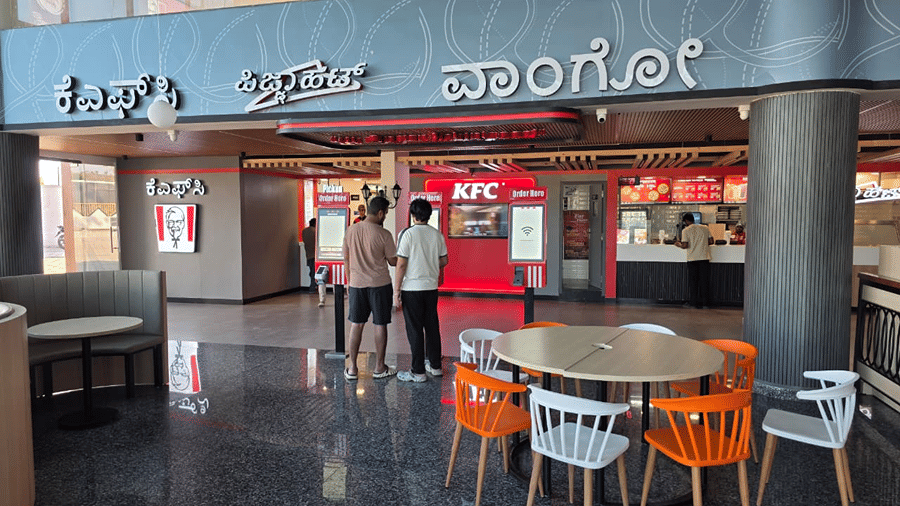Entrance to a food court area with a colourful signboard, round tables, and orange chairs for seating.
