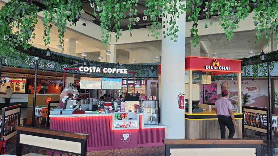 food court area decorated with hanging green plants overhead, with coffee and snack counters in view.