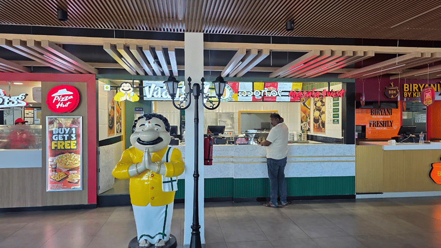 A food stall corner with a yellow mascot figure standing near the counter and a person placing an order.