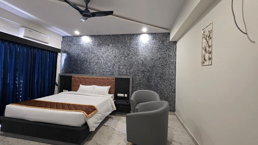 A simple guest room with a king size bed, a grey armchair beside it, and a ceiling fan overhead.