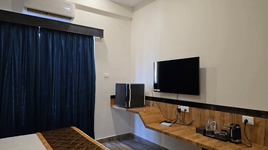 A room corner with a wall mounted TV, a wooden desk below it, and dark blue curtains near the window.