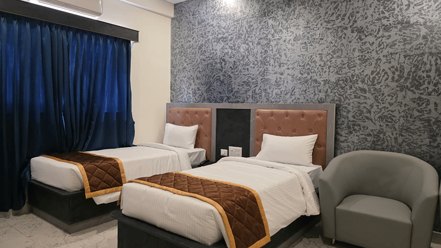 A room with two single beds, dark blue curtains, and a textured grey wall behind the headboards.