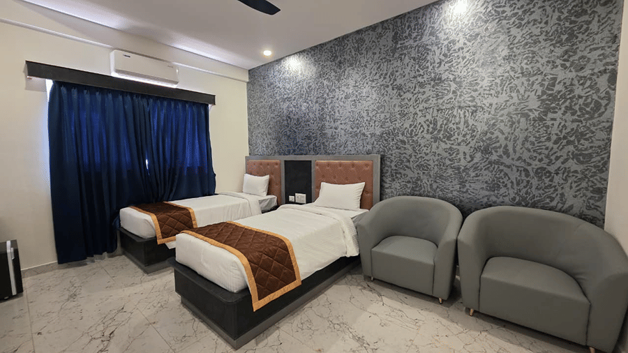A wide view of a twin bed room with two grey armchairs and a dark textured wall behind the beds.