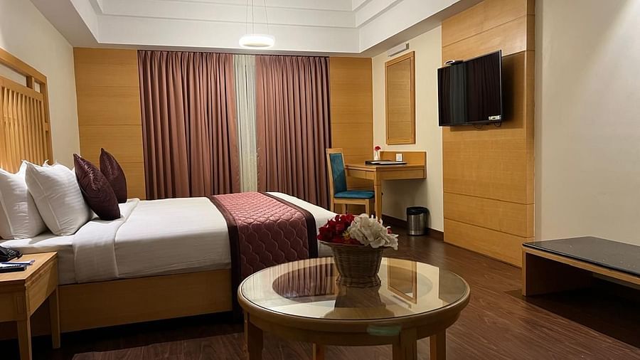 A spacious bedroom with a king-size bed, a sitting area with a sofa and coffee table, and large windows overlooking the city - MM Legacy, Kanchipuram.