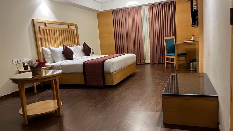 A corner view of the modern, well-lit bedroom with a king-size bed, a flat-screen TV, and a desk at MM legacy, Kanchipuram