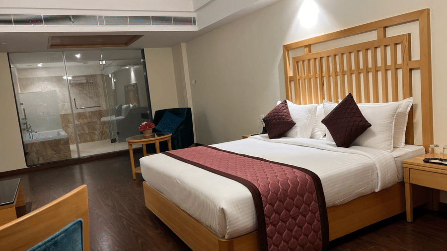 A luxurious bedroom with a king-size bed, a plush headboard, and a balcony with a view of the city - MM Legacy, Kanchipuram.