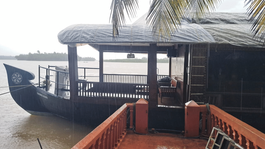 Traditional style wooden houseboat docked near a palm tree at Paradise Lagoon Resort, Udupi.