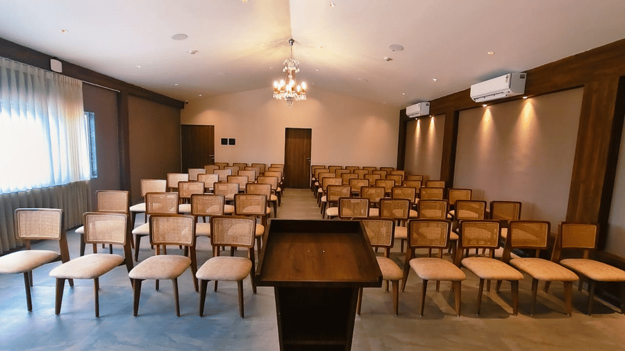 Rows of wooden chairs with padded seats facing a lectern in an event hall at Savyasaachii Hotel.
