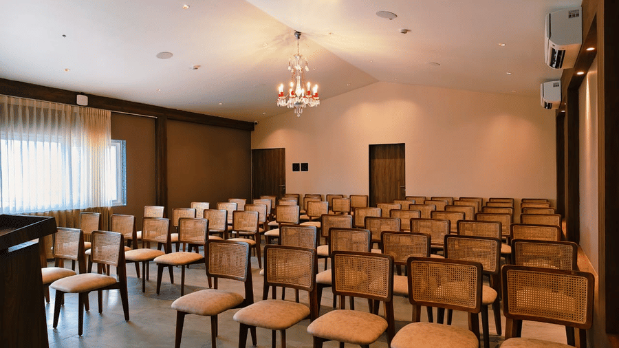 An event room arranged with multiple rows of wooden chairs facing forward under warm lights at Savyasaachii Hotel.
