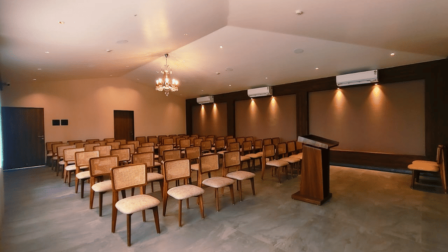 Rows of chairs with woven backs, set up for a presentation facing a wooden podium at Savyasaachii Hotel.