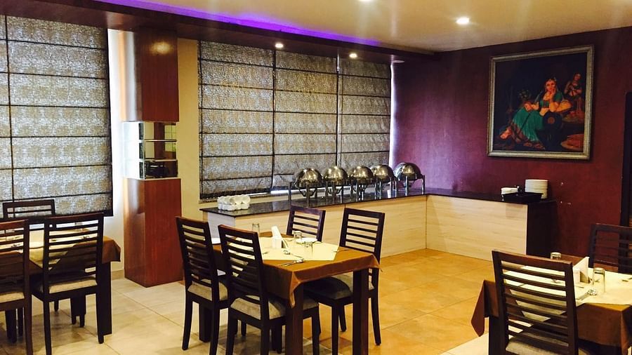 A dining room with a serene ambience, featuring a mix of wooden chairs and tables and a decorative screen - TGI Apple Inn, Jaipur 