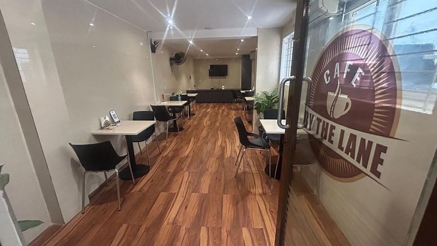 A dining area at The OnTime Hotel, Bangalore, with tables and chairs, and a sign that says CAFE BY THE LANE..
