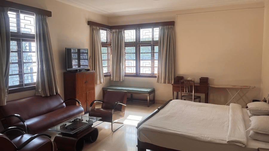 A broad look at a Superior room featuring a king size bed, a leather sofa set, and large windows with wooden frames | Trance Sunderban Resort
