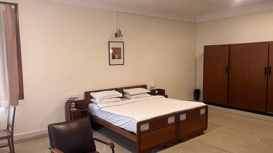 A view of the bed area flanked by a dark wood armchair and a large matching wardrobe against a plain wall | Trance Sunderban Resort