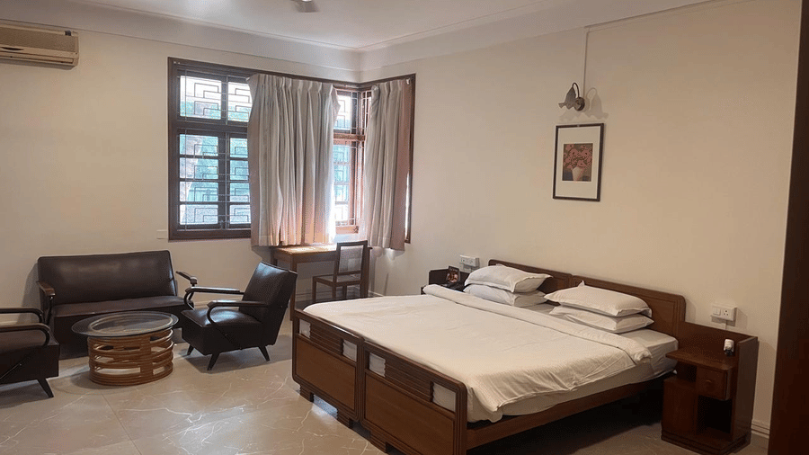 A bright room with a large bed, dark wood furniture, and a seating nook located under a window | Trance Sunderban Resort