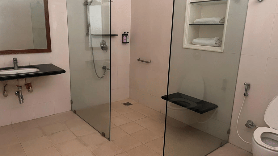 A view of the vanity area and walk-in shower separated by sleek glass panels, featuring minimalist tiling | Trance Sunderban Resort