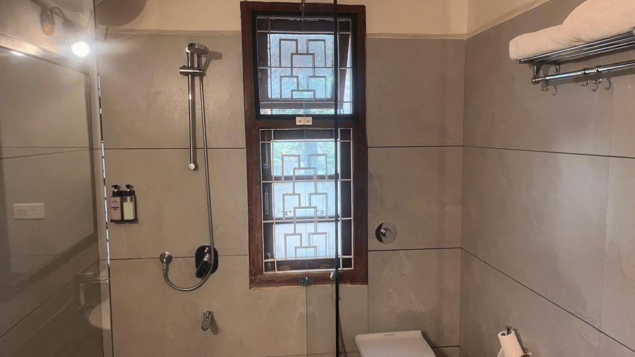A tiled bathroom featuring a wall-mounted shower head, a small frosted window, and a clean, contemporary toilet | Trance Sunderban Resort