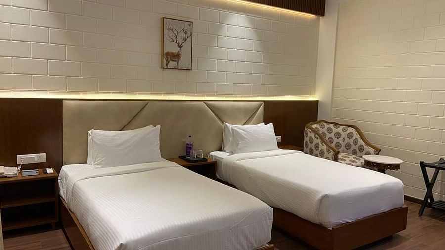 A bedroom with double bed, attached bathroom, framed wall art, round table and chair at Trishvam Symphony, Krishnagiri.