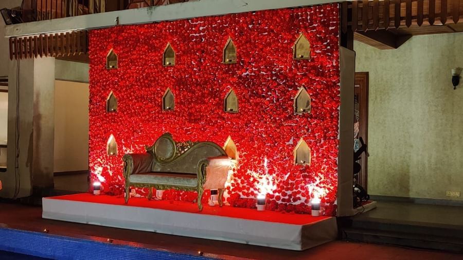 A red backdrop adorned with intricate patterns and a plush seating area forms a luxurious wedding stage setup
