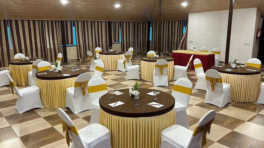An indoor banquet hall is prepared for an event, with round tables and chairs neatly arranged | Ballroom | Woodstock Resorts, Coorg