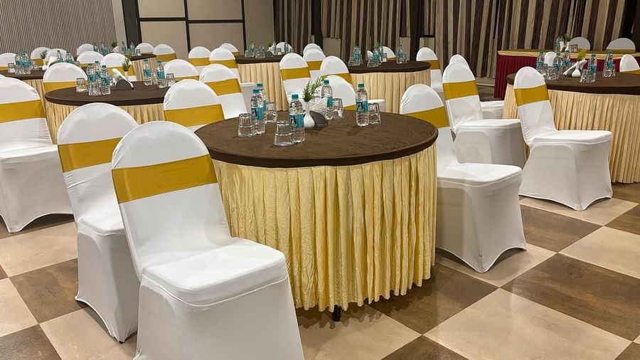 A closer view focuses on one of the round tables in the banquet hall, adorned with floral centrepieces and surrounded by chairs with white covers | Ballroom | Woodstock Resorts, Coorg