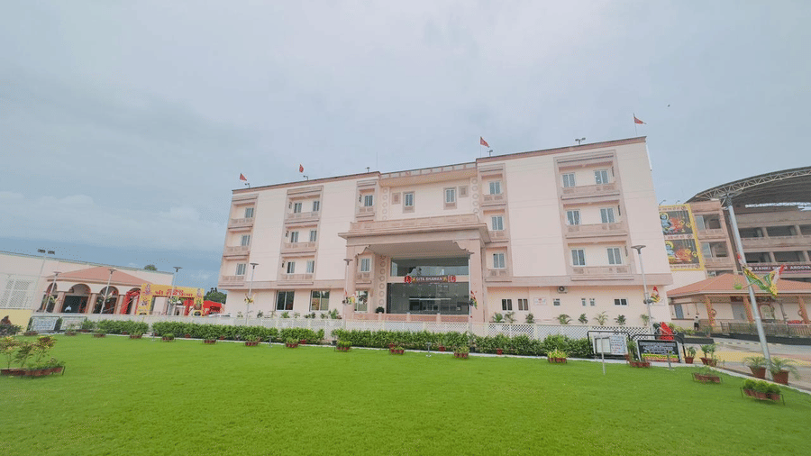 A wide view of a light-coloured building with a large green lawn - Kankidham Lords Inn