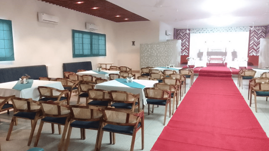 A spacious banquet hall set for an event with a red carpet and tables with blue accents facing the stage - Lords Eco Inn Belagavi