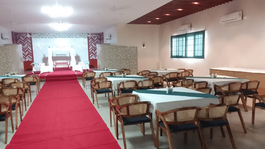 A spacious banquet hall with a red carpet isle leading through tables and chairs - Lords Eco Inn Belagavi
