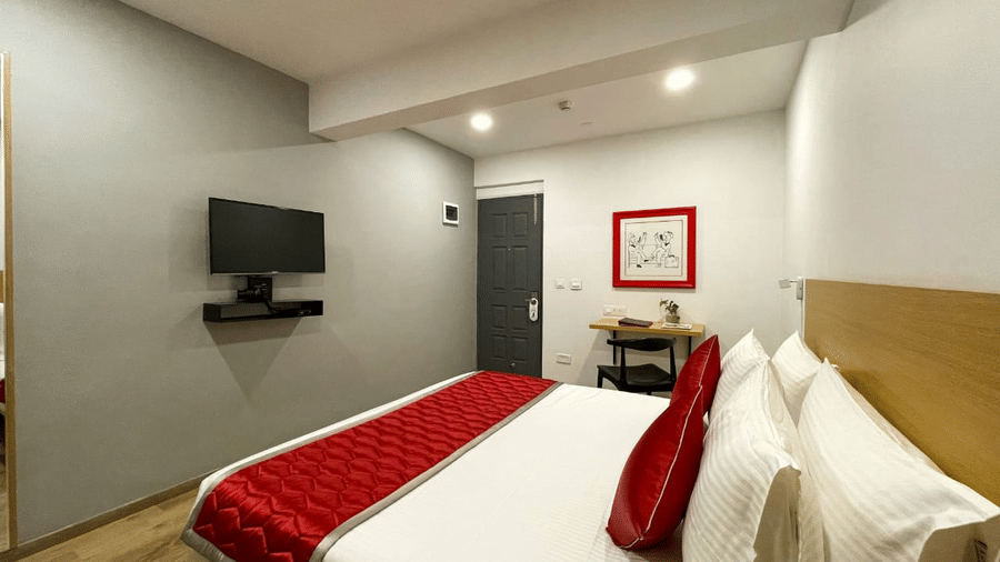 A cosy hotel room with a comfortable bed, a red bed runner, a flat-screen TV on the wall, and simple, modern decor - Lords Eco Inn Belagavi