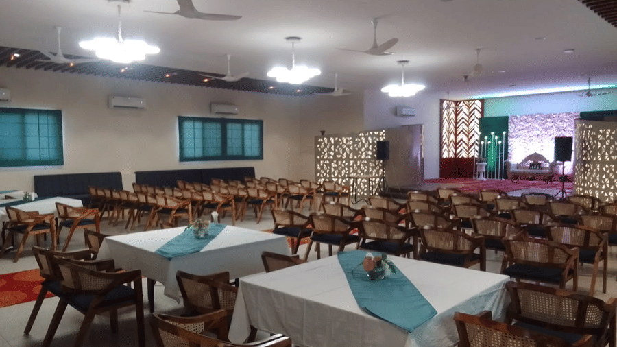 A spacious room with multiple tables covered in white cloth and set for dining - Lords Eco Inn Belagavi