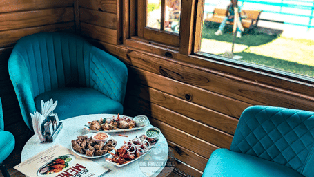 A dining setup at Dawat e Drung by FrozenFall Resort, Drung, Tangmarg, featuring 2 armchairs next to 1 small round table with food plates.