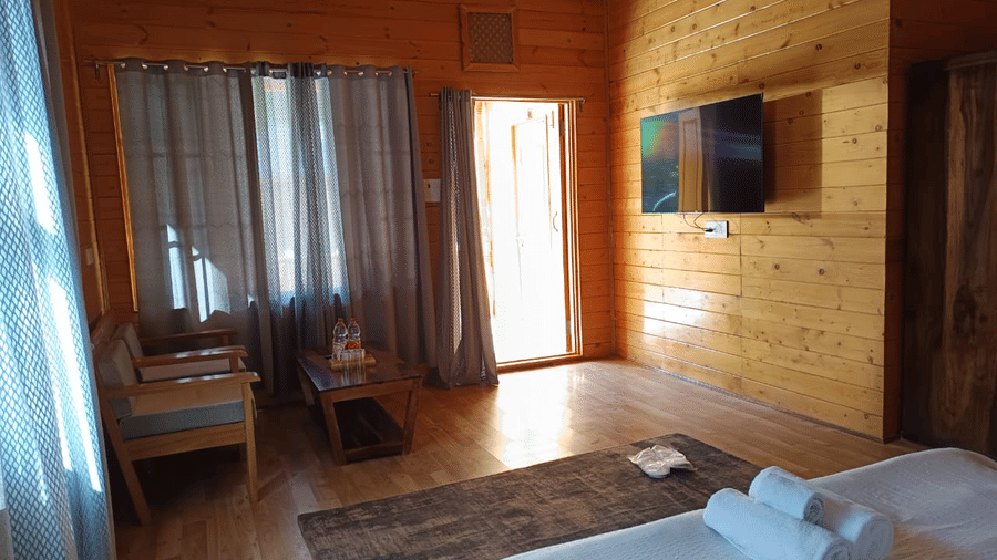 A bedroom at Dawat e Drung by FrozenFall Resort, Drung, Tangmarg, featuring 1 wall-mounted television, an armchair, curtains, and a double bed.