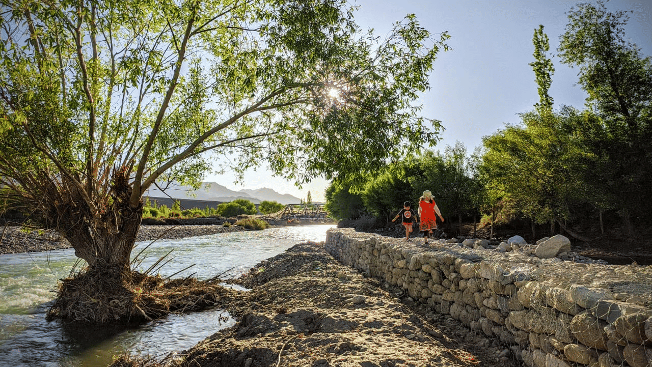 A flowing river running alongside a stone-reinforced bank with lush greenery at Indus Serenity Retreat.