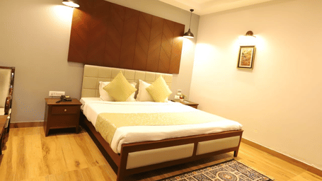 A bedroom with a king size bed, wood headboard panel, nightstand, and pendant lights at Amantra Shilpi Resort, Udaipur.