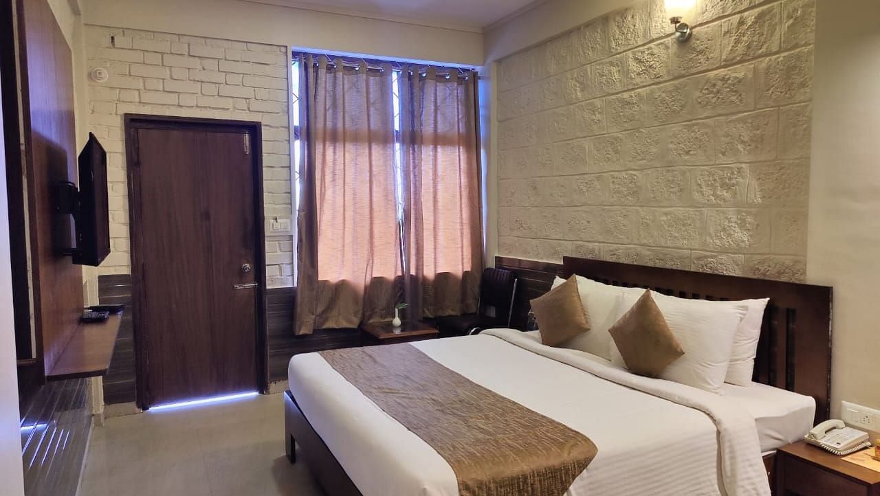 Bedroom with a huge bed, bedside table, windows with curtains, wooden door, and a TV | Standard Room | Woodstock Resorts, Coorg