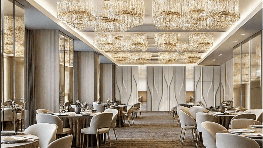 A large dining hall with several round tables and chairs under multiple ornate chandeliers