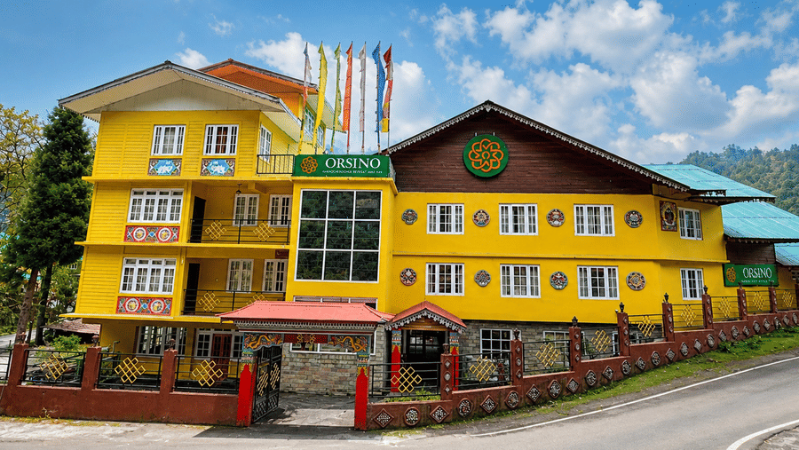 The front exterior of Orsino Khangri Karpo Retreat & Spa, Lachung under a clear sky showing the building name and architectural details from the street.
