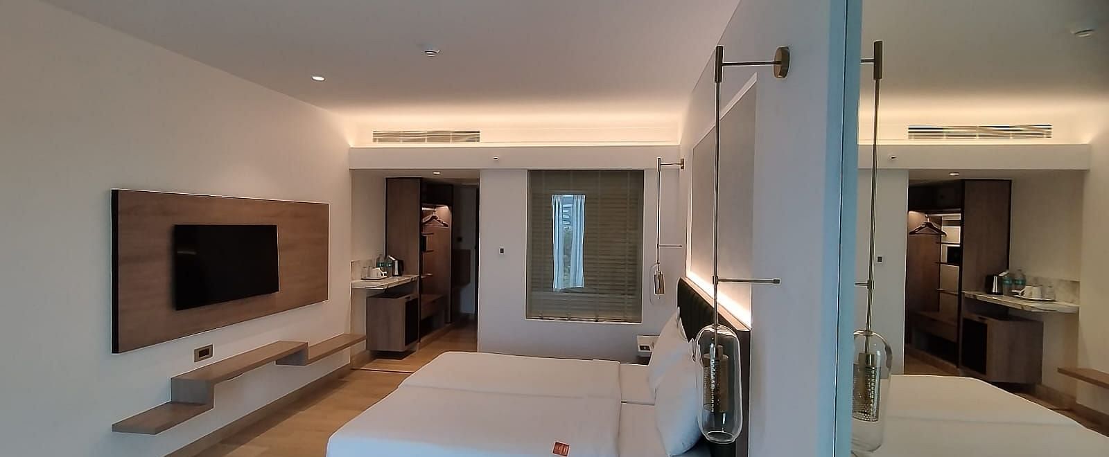 A modern executive room in Mirage Hotel, featuring twin beds with decorative head-rest, a large mirror, and a wooden panelled entertainment unit.