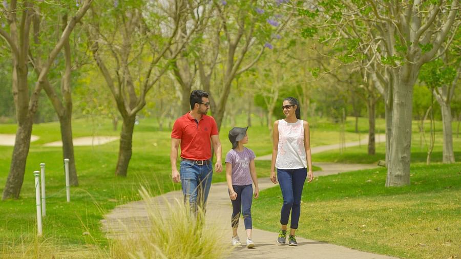 A family of three walking on a pathway next to manicured garden - Karma Lakelands.